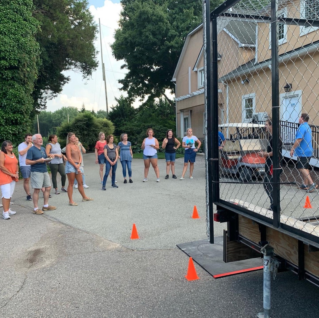 Guests gathering on an estate driveway at dusk beside the throwing cage